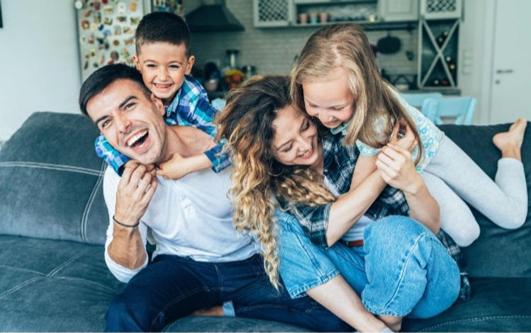 fostering in cambridgeshire Happy foster family laughing together on a sofa